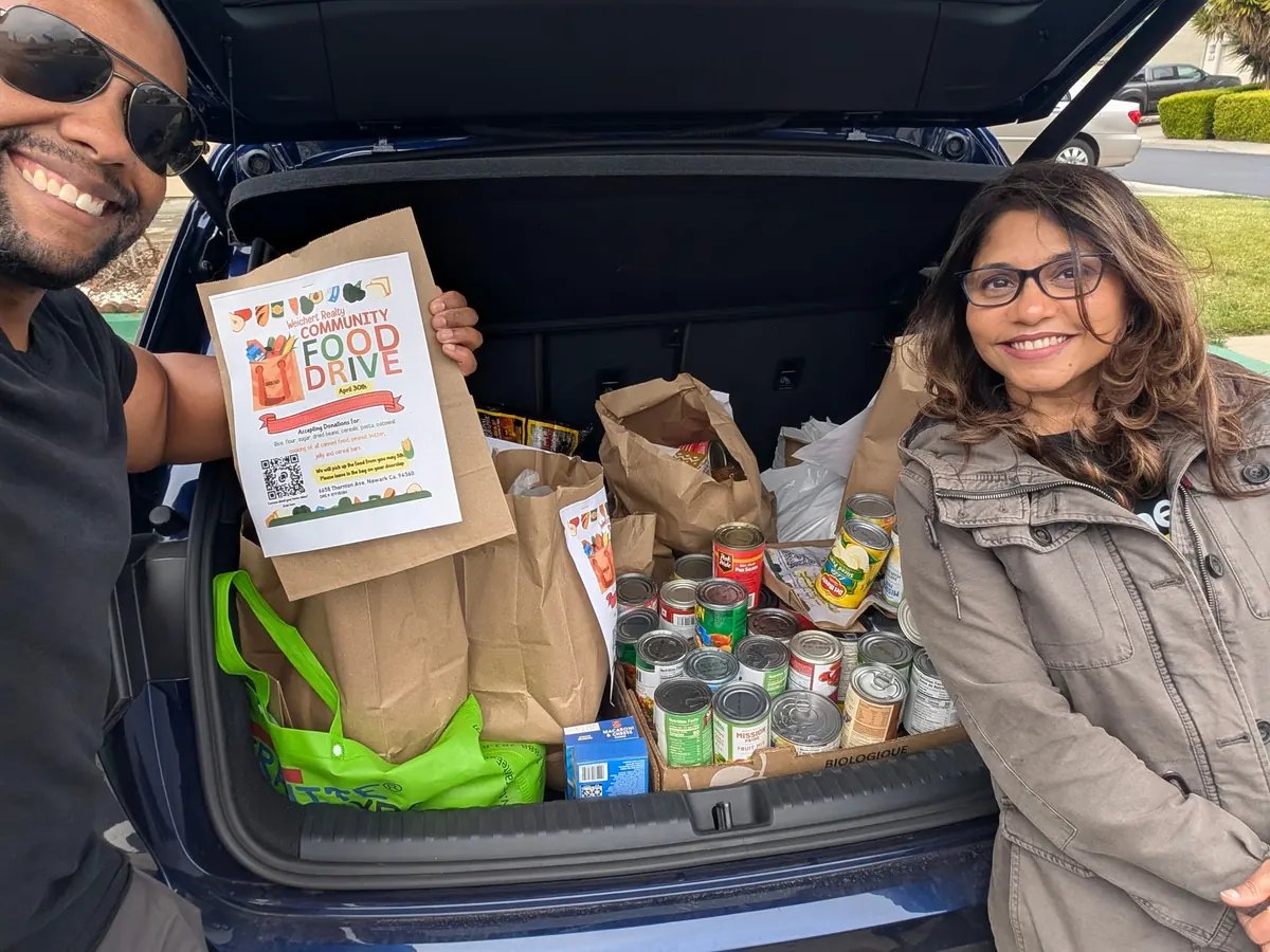 Two volunteers beside a car trunk filled with donated pantry goods